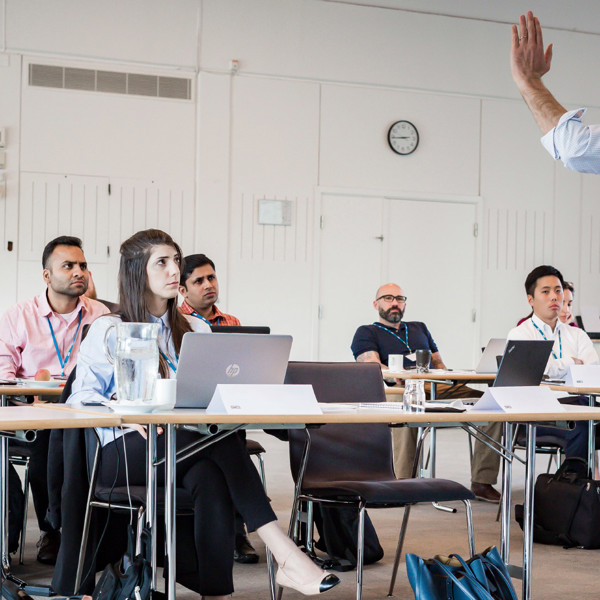 Man standing at the front of a classroom setting with course attendees watching him intently