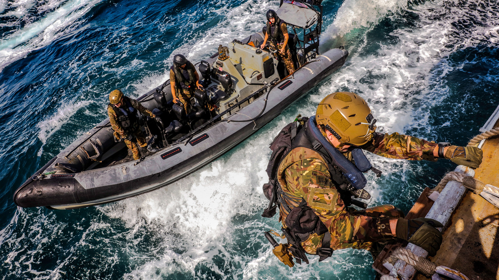 Military people climbing up a ship's ladder from a smaller boat